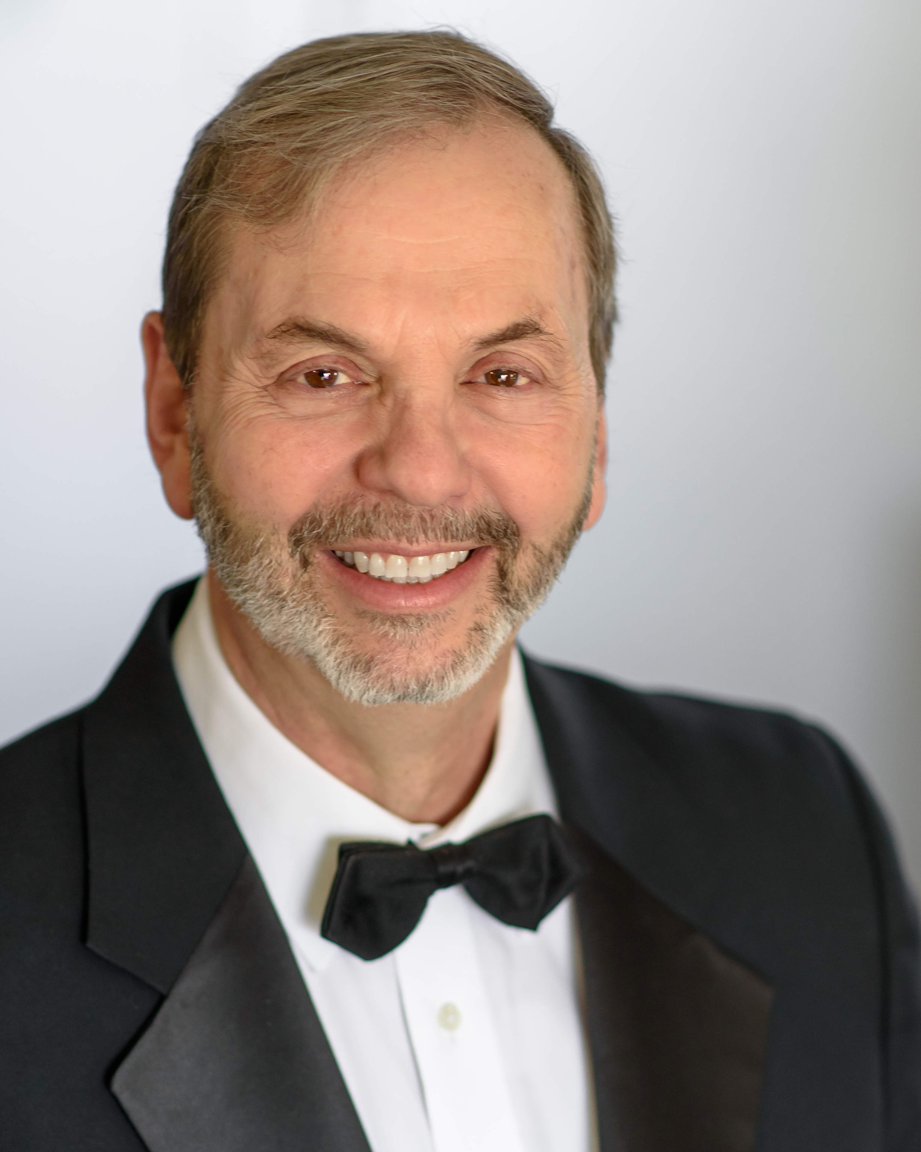 Headshot of Conductor Lou Kosma smiling, wearing a tuxedo and bow tie.
