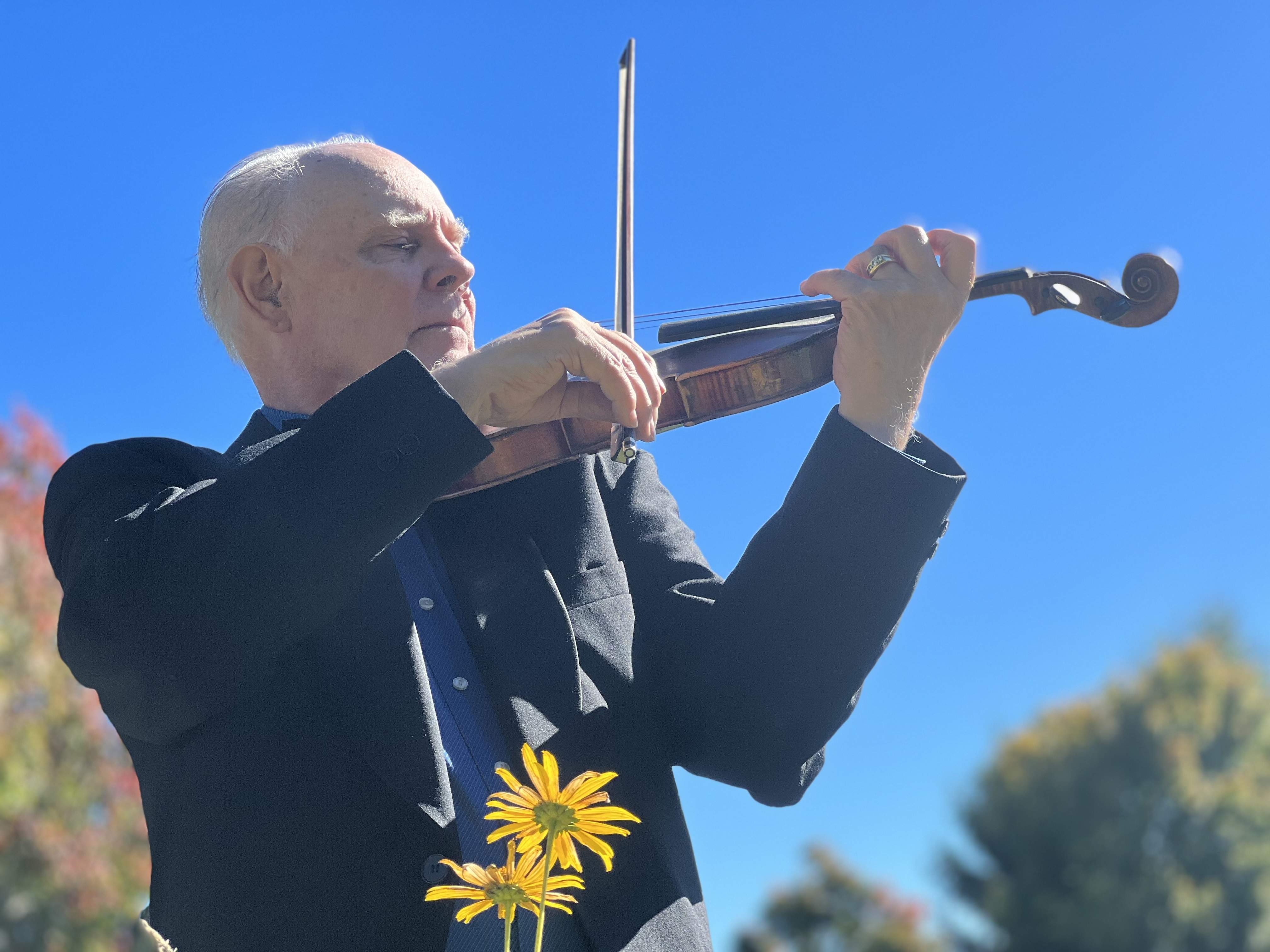 Concertmaster John Lindsay playing violin under a blue sky. Photo by Amornrat Lindsey
